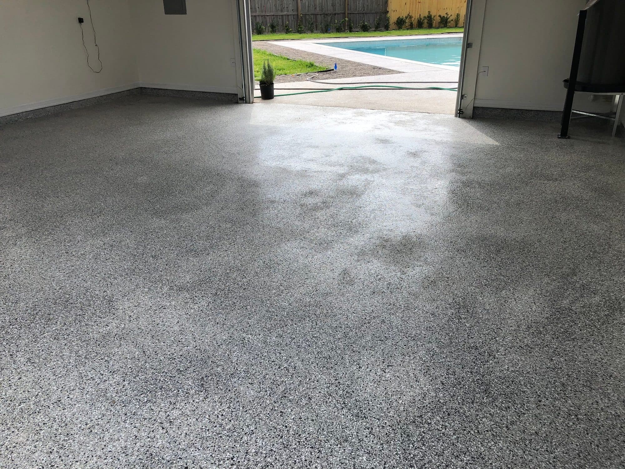 Grey speckled flake epoxy garage floor opening onto a backyard pool.