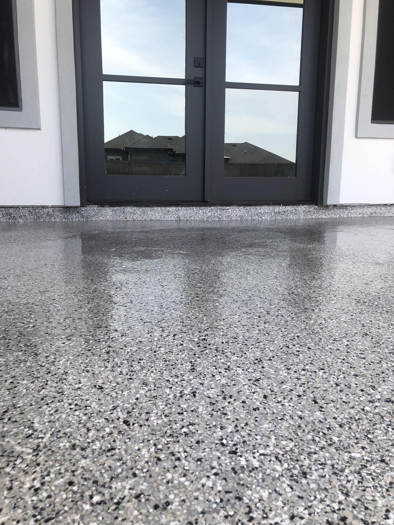 A fresh grey flake epoxy porch floor still wet-looking beside a home entry.